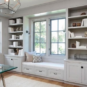 May include: A light gray home office with built-in bookshelves, a window seat, and a glass-top desk. The bookshelves are filled with white books and decorative items. The window seat has pillows. A geometric light fixture hangs from the ceiling.
