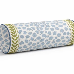 May include: A cylindrical bolster pillow with a white background and a pattern of light blue shapes. The ends are trimmed with a green leaf design and a blue border. This decorative pillow is a home decor item.