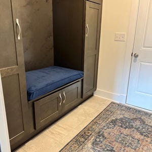 May include: A built-in entryway storage unit with dark gray cabinets, a blue cushion bench, and silver handles. The unit includes hooks for hanging items. A patterned rug lies on the floor.