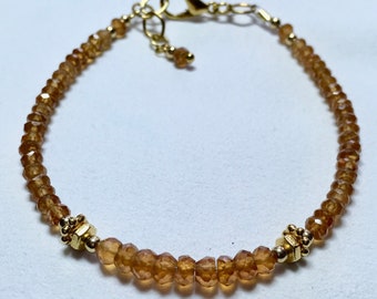 May include: A gold bracelet with a clasp closure and a row of brown gemstone beads.