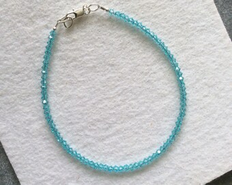 May include: A delicate blue crystal bracelet with a silver clasp. The bracelet is made of small, faceted crystals that are strung together on a thin silver chain.