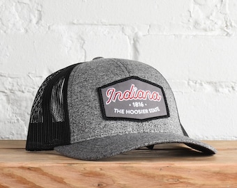 Puede incluir: Una gorra de camionero de malla gris y negra con un parche que dice "Indiana - 1816 - The Hoosier State".