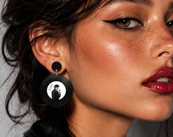 May include: Black vinyl record earrings with a circular design featuring a man holding a rose. The earrings have a black stud at the top and a silver-colored hook. The text "The Romance" is visible on the record.