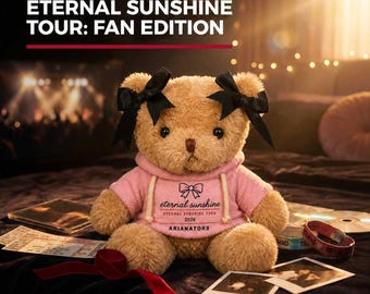 May include: A tan plush teddy bear wearing a pink hooded sweatshirt with a bow graphic and the text "eternal sunshine ETERNAL SUNSHINE TOUR 2026 ARIANATORS". The bear has two black satin bows attached to its ears and dark brown eyes.