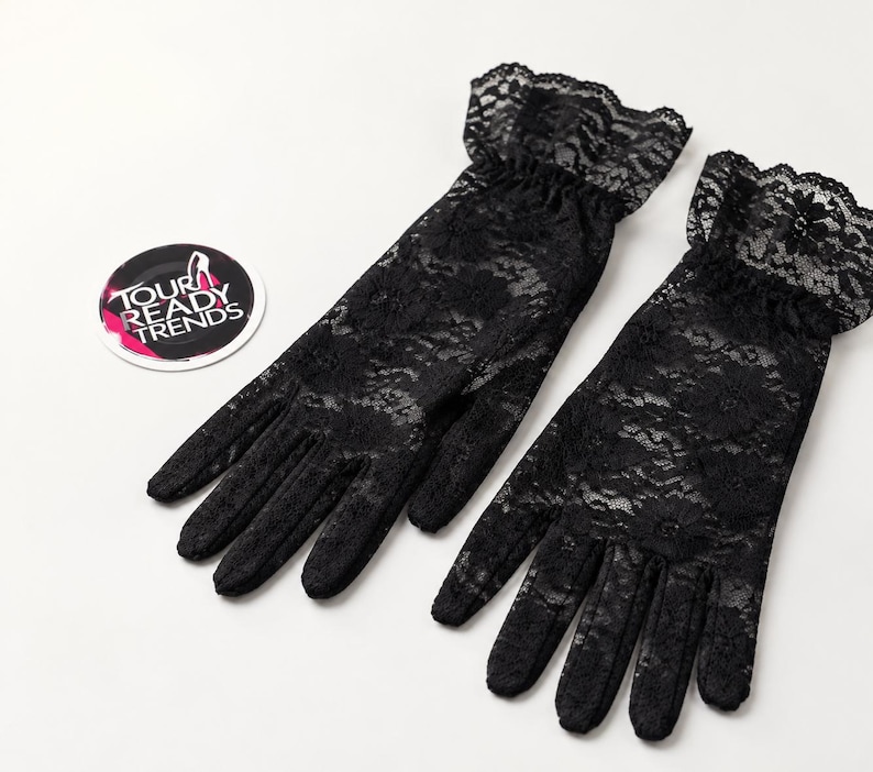 Puede incluir: Un par de guantes de encaje negro con un patr&oacute;n floral y un pu&ntilde;o con volantes en la mu&ntilde;eca. Junto a los guantes hay una pegatina circular con el texto TOUR READY TRENDS y un gr&aacute;fico de un zapato de tac&oacute;n en blanco, rosa y negro.