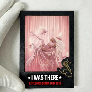 May include: A framed print featuring a pink-themed image of a person in a performance pose. The print has the text "I WAS THERE" and "LITTLE MISS DRAMA TOUR 2026". A gold-colored microphone graphic is on the frame.