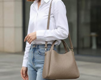 Peut inclure: Un sac à main taupe à la surface texturée, doté de deux anses courtes et d'une longue bandoulière réglable. Le sac présente une forme trapézoïdale structurée avec une base large et une ouverture supérieure légèrement incurvée, dans un ton neutre.