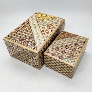 Könnte beinhalten: Zwei Holz-Puzzleboxen mit komplizierten Mosaikmustern in Braun-, Beige- und Gelbtönen. Die größere Box ist rechteckig, und die kleinere Box ist ebenfalls rechteckig. Die Boxen werden auf einer weißen Oberfläche präsentiert.
