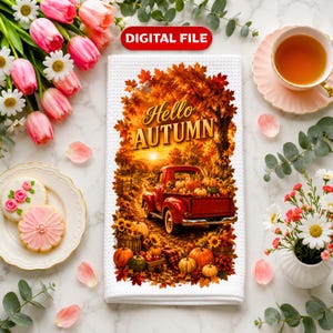 May include: A white waffle-textured kitchen towel featuring a digital print of a red pickup truck loaded with pumpkins on a dirt road, surrounded by autumn foliage and sunflowers. The text reads Hello AUTUMN in gold letters above the truck.