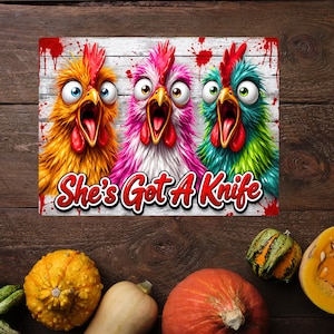 Puede incluir: Un letrero rectangular con tres pollos de dibujos animados con ojos muy abiertos y picos abiertos sobre un fondo de tablones de madera blanca con salpicaduras de pintura roja. El texto "She's Got A Knife" aparece en letras rojas.