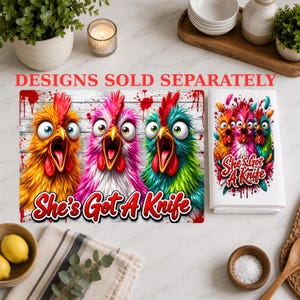 Puede incluir: Un pa&ntilde;o de cocina rectangular y una impresi&oacute;n a juego con tres pollos de ojos muy abiertos, coloridos en amarillo, rosa y verde azulado con crestas rojas. El dise&ntilde;o incluye salpicaduras de pintura roja y el texto She's Got A Knife.