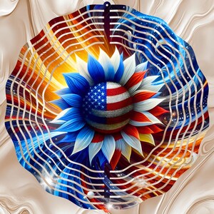 May include: A decorative metal wind spinner featuring a sunflower design with the American flag. The flower's petals are blue, red, and white, with the center displaying the flag's stars and stripes. The background has a wavy pattern.