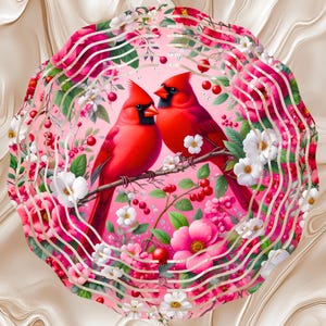 May include: A digital illustration of two red cardinals perched on a branch, surrounded by pink and white flowers, berries, and green leaves. The birds are facing each other, set against a pink background with a decorative border.