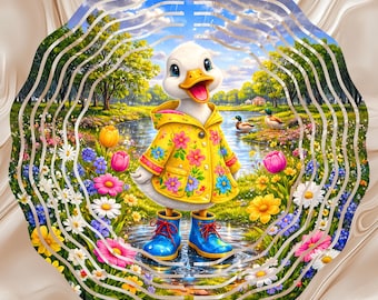 May include: A circular metal wind spinner featuring a colourful illustration of a white duckling wearing a yellow floral raincoat and blue rain boots, standing in a puddle surrounded by vibrant wildflowers, green trees, and a pond with two ducks.