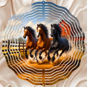 May include: A circular metal wind spinner featuring a printed scene of three horses running on a dirt path. Two horses are brown with white facial markings and one is black. A red barn and a wooden fence are visible in the background.