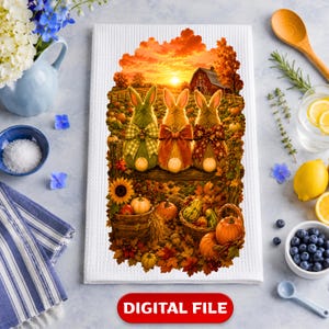Puede incluir: Un paño de cocina blanco con textura de gofre que presenta una ilustración impresa de tres conejos sentados en una valla al atardecer. La escena incluye un granero rojo, hojas de otoño, girasoles y cestas llenas de calabazas en tonos naranjas.