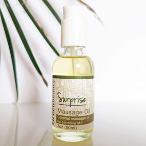 May include: A clear glass bottle with a white pump top and a green and white label that reads "Surprise Massage Oil Coconut massage oil for sensitive skin 2oz (60ml)"