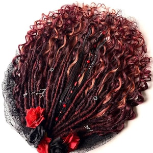 May include: A burgundy and auburn dreadlock wig with curly ends, adorned with black lace, red and black roses, and silver charms. The wig features a black leather band with red beads.