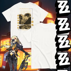 May include: White t-shirts with a graphic design featuring a character illustration and text. One shirt displays the design on the front, while another shows the back with additional text and a topographic map-like design. The shirts are part of a themed collection.