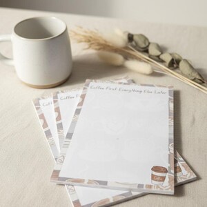 May include: A stack of rectangular paper notepads featuring a light brown and white coffee-themed border with the text Coffee First. Everything Else Later at the top and a small coffee cup illustration in the bottom right corner of each sheet.