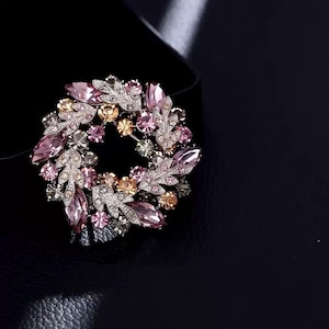 May include: A silver-toned brooch with a floral design. The brooch is made of metal and features pink, purple, and gold rhinestones.