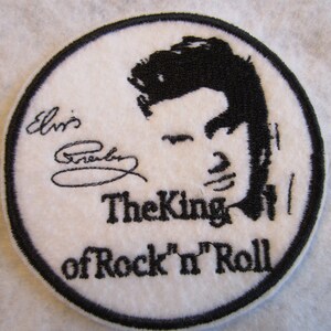 May include: White embroidered patch with a black silhouette of Elvis Presley's face and the text "Elvis Presley The King of Rock 'n' Roll".