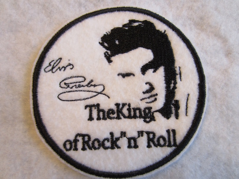 May include: White embroidered patch with a black silhouette of Elvis Presley's face and the text "Elvis Presley The King of Rock 'n' Roll".