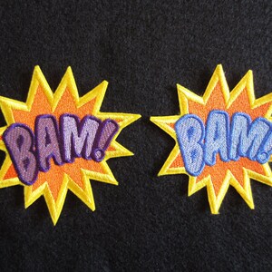 May include: Two yellow starburst-shaped patches with the word "BAM!" in purple and blue lettering.