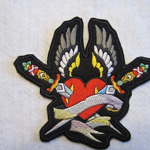 May include: Black embroidered patch with a red heart pierced by two daggers, surrounded by a banner and two wings.