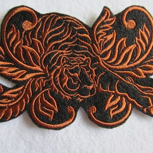 May include: A brown embroidered patch with a tiger design surrounded by intricate floral patterns on a black background.