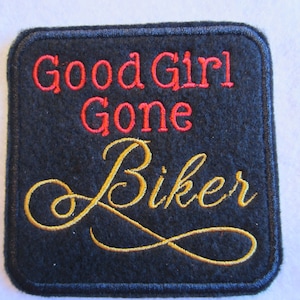 May include: Black square patch with red embroidered text "Good Girl Gone Biker" in a cursive font. The word "Biker" is in gold thread.