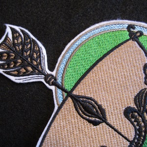 May include: Embroidered patch with a brown bow and arrow design. The arrow has a brown and black feathered fletching. The bow is surrounded by a green circle with a blue and white border.