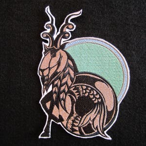 May include: Black and brown embroidered patch of a goat with horns and a tail, with a green and blue circle behind it.