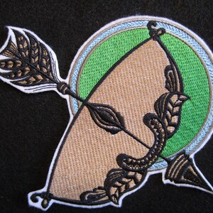May include: Embroidered patch featuring a brown and black bow and arrow with a green and blue circle background.