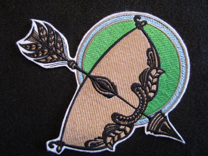May include: Embroidered patch featuring a brown and black bow and arrow with a green and blue circle background.