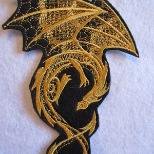 May include: Gold embroidered dragon patch on a black felt background. The dragon is curled up with its wings spread out.