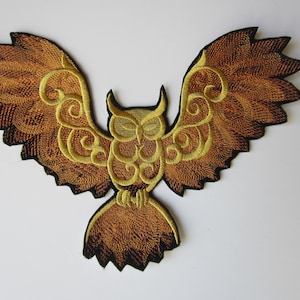 May include: Embroidered iron-on patch of a golden owl with brown wings spread wide. The owl has intricate details and a stylized design.