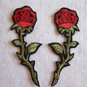May include: Two red embroidered rose patches with green leaves and black stems. The roses are in a classic style with a detailed design.