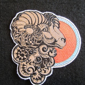May include: Embroidered patch featuring a detailed black and brown ram's head with intricate designs. The ram's head is set against a red circle with a blue and white border.