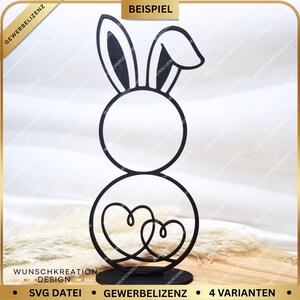 Könnte beinhalten: Schwarze Osterhasen-Dekoration aus Metall. Der Hase hat große Ohren und einen kreisförmigen Körper. Zwei ineinander verschlungene Herzen bilden den Unterkörper. Die Basis ist eine kleine, rechteckige Form. Der Text "WUNSCHKREATION DESIGN" ist sichtbar.