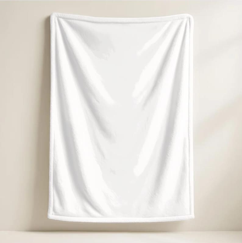 Back view product mockup displaying the plain solid white fleece backing of a custom plush throw blanket for the Elliot design from the Roblox game Forsaken by KraftilyEm. Shows the soft, fluffy textured white lining with finished hemmed edges hanging against a neutral beige wall. Highlights the high-quality cozy material and construction of the gamer throw. An essential detail shot for buyers evaluating custom Roblox fan art merchandise and cozy bedroom decor accessories.
