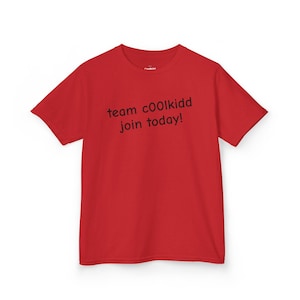 Op de afbeelding: Een rood t-shirt met de zwarte tekst "team c00lkidd join today!". Het shirt met korte mouwen is effen van kleur. De tekst is in een informeel lettertype.