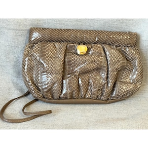 May include: A brown snakeskin-patterned clutch with a gold-colored clasp. The clutch has a gathered design and a long, thin strap. The bag is made of a textured material and has a rectangular shape.