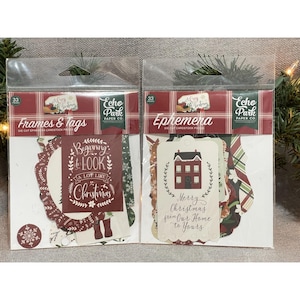 Puede incluir: Dos paquetes de efímeras y marcos y etiquetas troqueladas con temática navideña. Un paquete presenta un marco burdeos con el texto "Beginning to Look a Lot Like Christmas". El otro paquete tiene etiquetas con un gráfico de una casa y el texto "Merry Christmas from Our Home to Yours."