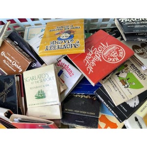 May include: A selection of vintage matchbooks, each with unique designs and text. The matchbooks display logos for restaurants and businesses, such as "Monterey Jacks," "Northwest Spirit," and "Sgarlato's at the Seaport." The color palette includes red, yellow, and black.