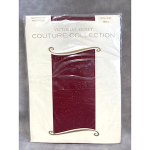 Può includere: Confezione sigillata di collant Victoria's Secret Couture Collection Nightlights in Royal Ruby. La confezione è bianca con il nome del marchio e i dettagli del prodotto stampati in nero. I collant sono di colore rosso scuro.
