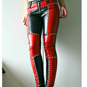 May include: Black and red leather trousers with silver stud detailing. The trousers have a colour-blocked design with black and red panels, and a zip closure. They are worn with black high-heeled boots with silver studs.