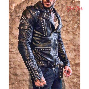 Könnte beinhalten: Schwarze Lederjacke mit silbernen Nieten und Reißverschlüssen. Die Jacke hat einen klassischen Biker-Stil mit Reverskragen, mehreren Taschen und einem Gürtel. Die Ärmel sind lang und haben Reißverschlussdetails. Ein auffälliges Kleidungsstück.