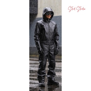 Puede incluir: Mono de cuero negro con capucha y gafas. El traje de una pieza tiene cierre de cremallera y se usa con guantes y botas. La imagen est&aacute; tomada al aire libre bajo la lluvia. El logotipo de Stud Studio est&aacute; en la esquina superior derecha.