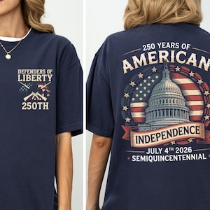 May include: Navy blue t-shirt with "Defenders of Liberty" and "250th" on the front. The back features a design commemorating 250 years of American Independence, including the Capitol building, the American flag, and the date July 4th, 2026.